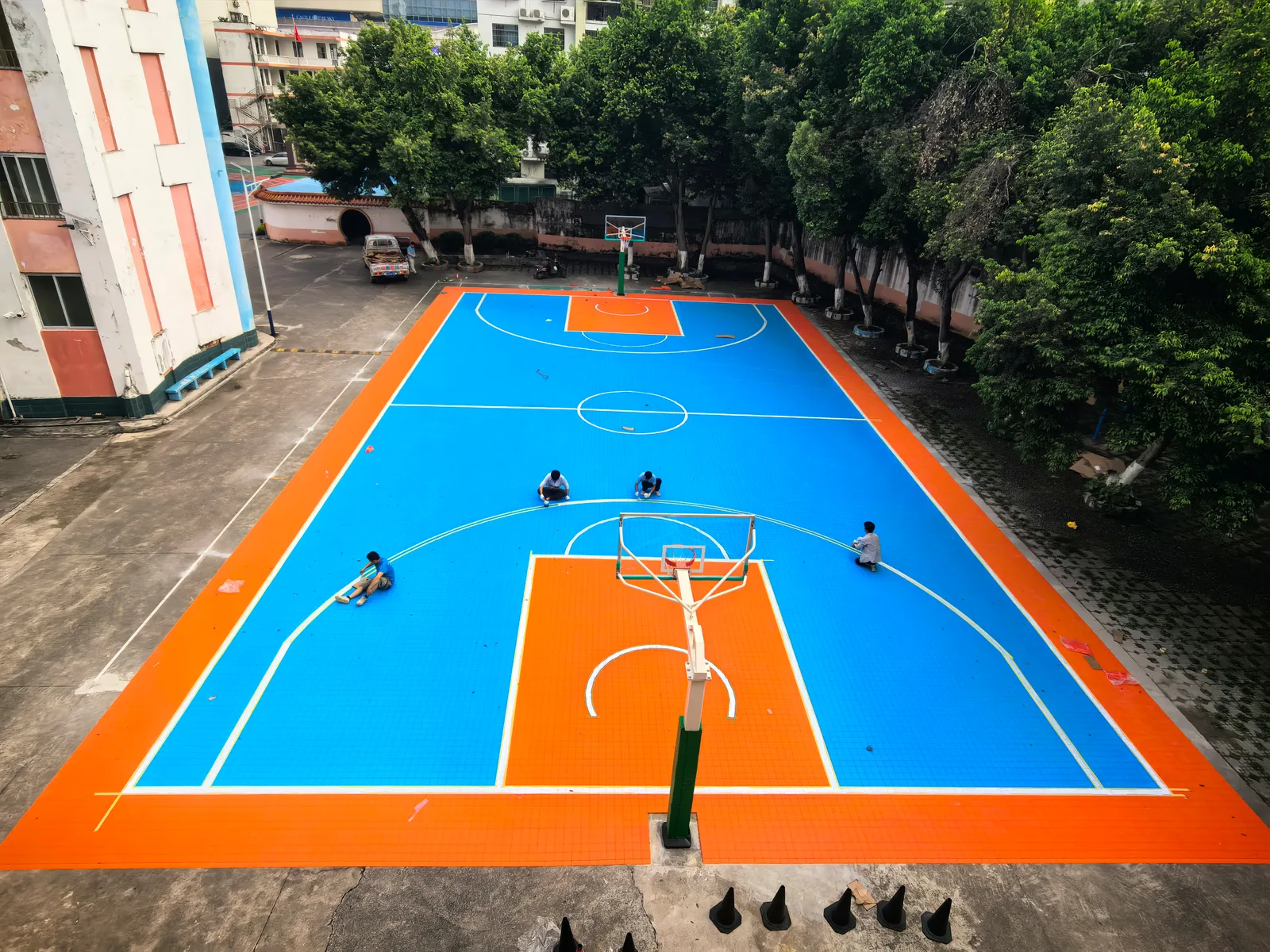 Workers installing interlocking tiles on an outdoor basketball court