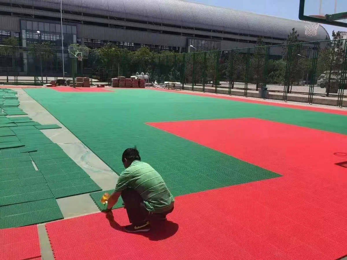 An installer connecting red and green interlocking flooring sections on a basketball court